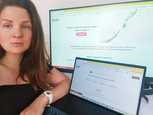 Une femme assise à son bureau devant un ordinateur portable et un écran affichant la plateforme Opale destinée aux salariés victimes de violences conjugales