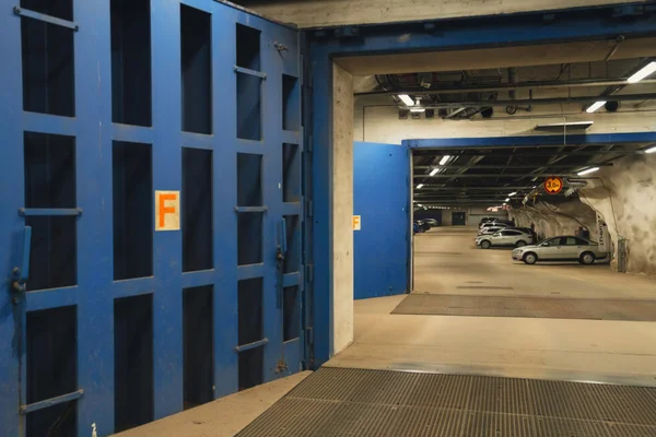 Énorme porte anti-bloc bleue métallique entrouverte sur un parking souterrain, accès sécurisé d'un abri antiatomique géant en Finlande
