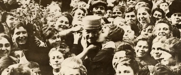 Foule de femmes souriantes entourant un homme en casquette militaire lors de l'armistice de la Première Guerre mondiale, une femme l'embrassant sur la joue
