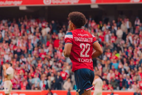 Tiago Santos de dos, portant le maillot rouge du LOSC numéroté 22, debout sur la pelouse face aux spectateurs flous du stade
