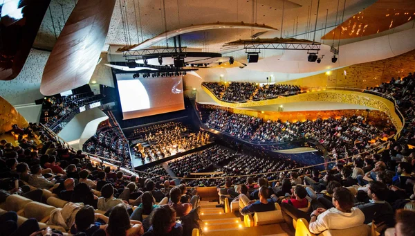Salle de concert moderne remplie de spectateurs assistant à un ciné-concert, avec un grand écran et un orchestre en pleine représentation sur scène