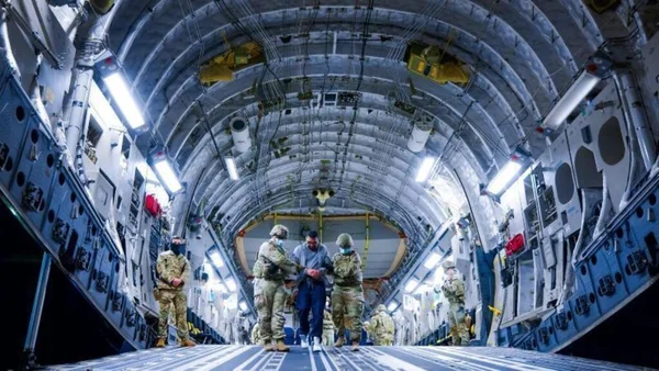 Intérieur d'un avion cargo militaire américain avec des agents en uniformes de camouflage et masques se tenant sur la rampe arrière, lors de l'arrivée d'un déporté à El Salvador. Elmer Concepcion Romero Janes descend de l'avion dans des images diffusées par le gouvernement salvadorien.
