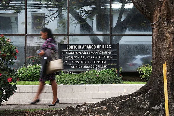 Une passante marche devant l'enseigne de l'Édificio Arango Orillac listant le cabinet Mossack Fonseca et ses entités, devant un bâtiment aux vitres réfléchissantes à Panama