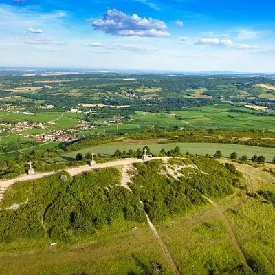 Vue aérienne du Mont de Sène dit Les Trois Croix à Dezize-lès-Maranges, colline herbeuse surmontée de trois croix de pierre dominant les champs, forêts et le village sous un ciel bleu nuageux