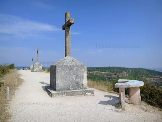 Rangée de croix de pierre sur un chemin de gravier surplombant un paysage vert sous un ciel bleu dégagé, la montagne des Trois Croix en Bourgogne