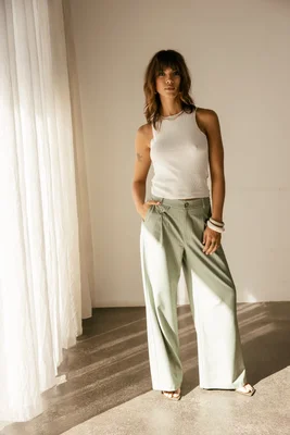 Photo en pied d'une femme dans une pièce baignée de lumière portant le pantalon large vert clair à pinces Alison Looney avec un haut blanc sans manches