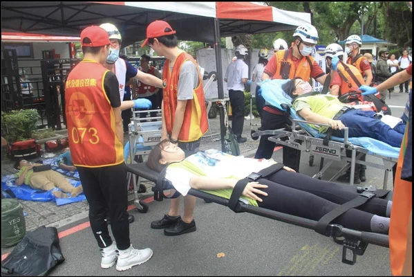 Des secouristes taïwanais en gilets rouges marqués d'une croix rouge et orange portant secours à des victimes simulées sur des brancards lors d'un exercice de protection civile