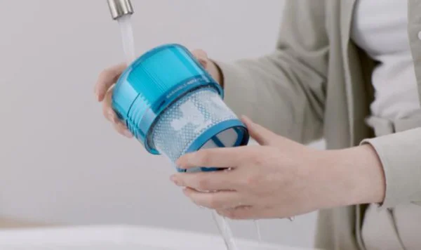 Main tenant un filtre cylindrique bleu d'aspirateur Dyson sous un robinet pour le rincer sous l'eau courante