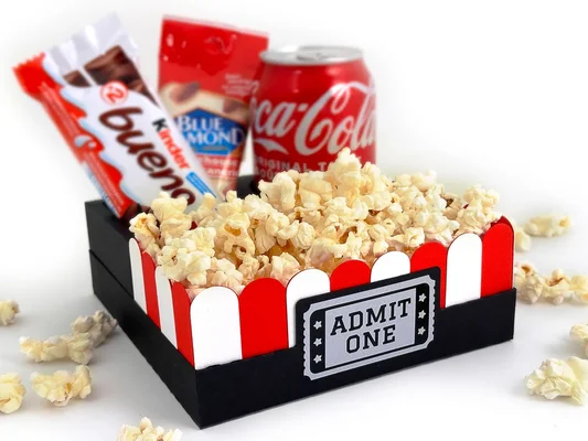 Boîte de snacks sur le thème du cinéma remplie de pop-corn, accompagnée d'une barre Kinder Bueno, d'un sachet d'amandes Blue Diamond et d'une canette de Coca-Cola