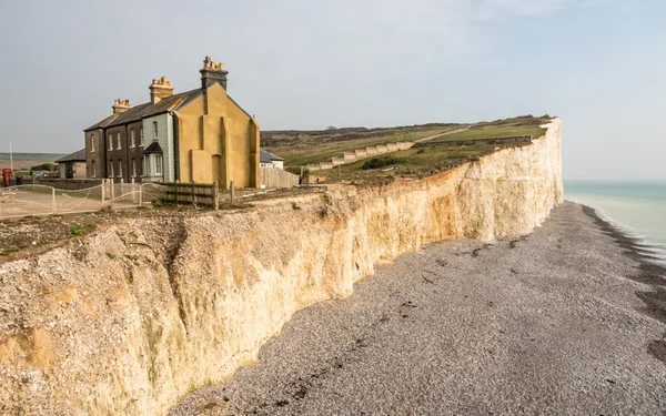 Rangée de maisons construites au bord d'une falaise de craie en cours d'effondrement, surplombant une plage de galets et la mer dans le cadre d'un paysage côtier menacé par l'érosion