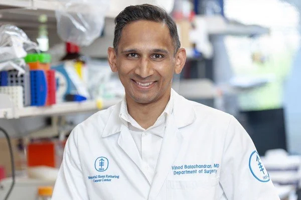Vinod P. Balachandran, chirurgien hépatopancréatobiliaire du Memorial Sloan Kettering Cancer Center, souriant en blouse blanche dans un laboratoire aux étagères garnies d'équipements