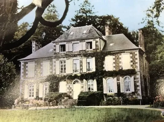Carte postale du château des Noyers au Tourneur : grande demeure en pierre à plusieurs étages, toit d'ardoise, volets blancs et façade partiellement couverte de lierre, derrière une pelouse arborée.