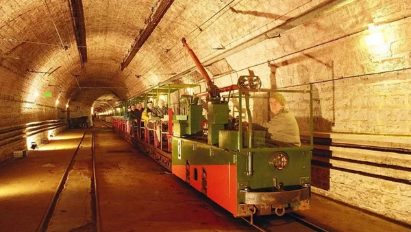 Petit train vert et rouge transportant des visiteurs dans le long tunnel voûté du fort du Hackenberg, éclairé par des lumières chaudes.