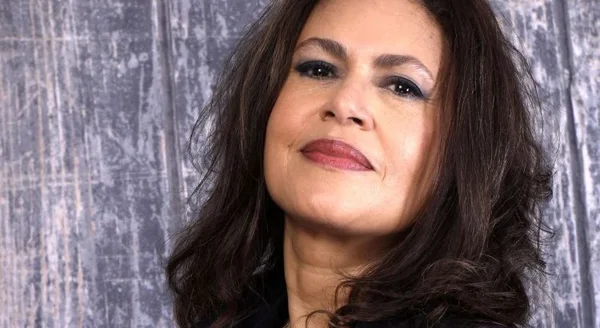 Portrait de Viktor Lazlo, chanteuse à la chevelure brune ondulée et au maquillage marqué, regard tourné vers le haut sur un fond gris texturé.