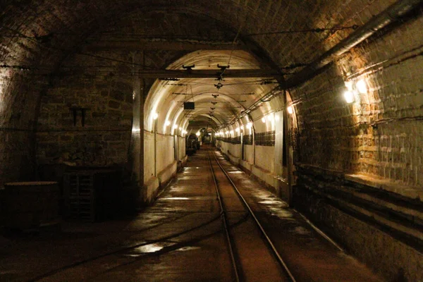 Galerie souterraine voûtée en briques de l'ouvrage A19 du Hackenberg, avec une voie ferrée centrale et un éclairage mural dans une ambiance sombre.