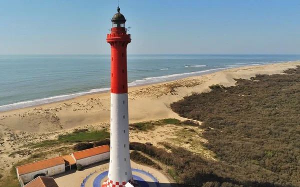 Photographie aérienne du phare de la Coubre, le plus haut phare du département de La Charente-Maritime, perché sur une côte sablonneuse avec des dunes et de la végétation, surplombrant l'estuaire de la Gironde.