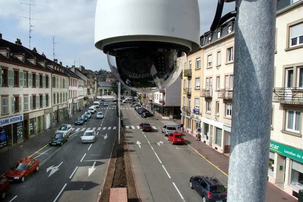 Vue plongeante depuis une caméra de vidéosurveillance sur une rue animée de Sarreguemines, bordée d'immeubles et de voitures garées.