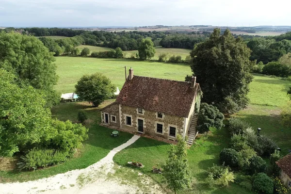Maison de campagne en pierre avec toit tuilé rouge située dans un paysage rural verdoyant avec des champs et des arbres, à 2 heures de Paris