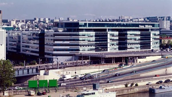 Le siège de France Télévisions dans le 15e arrondissement de Paris : bâtiment moderne aux façades vitrées bordé par la Seine, avec une voie rapide et des voies ferrées au premier plan