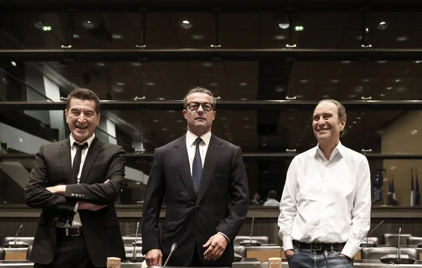 Xavier Niel et Matthieu Pigasse, en tenue formelle, debout côte à côte lors de leur audition devant la commission sur l'audiovisuel public, dans une salle moderne aux parois vitrées et gradins