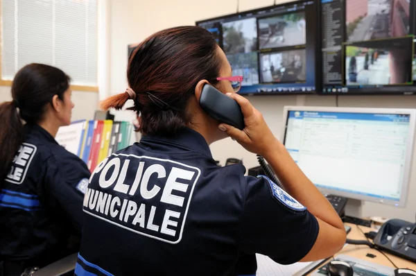 Deux agentes de police municipale dans un centre de supervision urbain ; celle au premier plan téléphone tout en surveillant des écrans de vidéosurveillance.