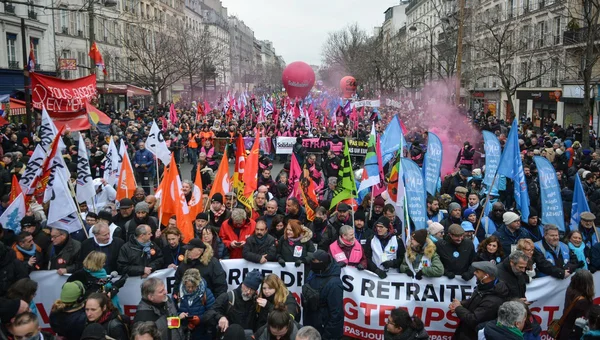Manifestation contre la réforme des retraites en France : foule dense de manifestants portant des drapeaux orange, bleus et blancs, banderelles "RETRAITE" et "TEMPS", fumigènes roses en arrière-plan.