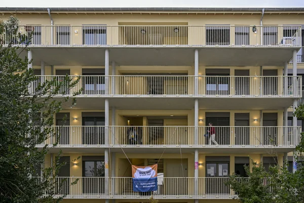 Immeuble résidentiel à plusieurs étages avec balcons, orné d'une banderole accrochée à un balcon inférieur, à la Maison de la diversité à Lyon.