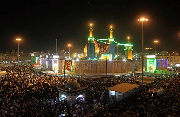 Des milliers de pèlerins chiites rassemblés de nuit sur une place devant le sanctuaire de l'imam Abbas à Karbala, éclairé par des dômes dorés et des minarets.
