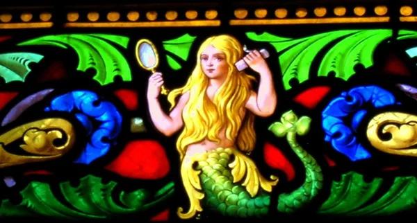 Vitrail représentant une sirène blonde aux cheveux dorés tenant un miroir de beauté et un peigne ornés de motifs décoratifs verts, bleus et rouges, inspiré du site du château de Fougères