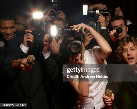 Groupe de photographes et journalistes en civil, armés de caméras et micros, encombrés dans un cadre sombre lors d'un événement de célébrité.