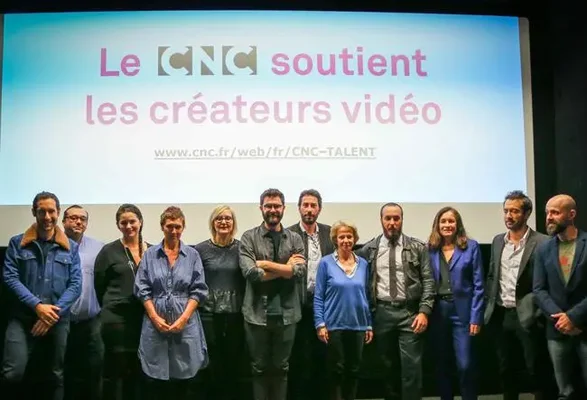 Un groupe d'une douzaine de personnes alignées sur une scène devant un grand écran de projection affichant le texte « Le CNC soutient les créateurs vidéo ».