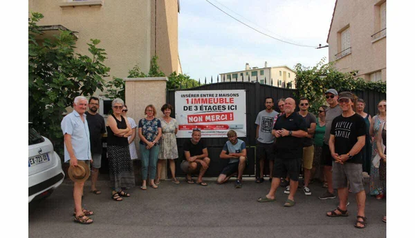 À Chenôve, une vingtaine de riverains posent devant un portail métallique noir avec une pancarte "INSÉRER ENTRE 2 MAISONS 1 IMMEUBLE DE 3 ÉTAGES ICI NON MERCI !"