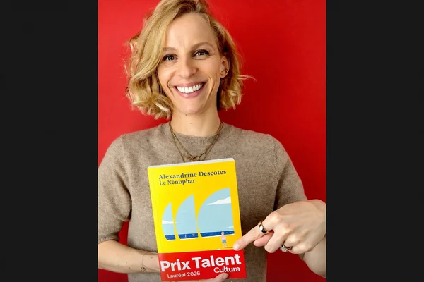 Alexandrine Descotes, femme blonde aux vagues cheveux, souriante, portant un pull beige, tenant un livre jaune intitulé 'Le Nénuphar' sur fond rouge. Le livre porte une bannière rouge 'Prix Talent Cultura Lauréat 2026'.