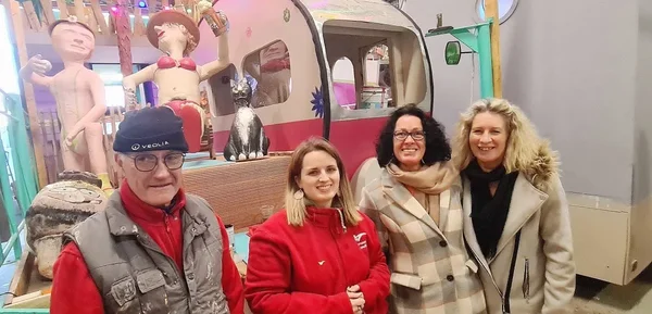 Quatre personnes (un homme et trois femmes) posant devant un décor coloré avec des figurines géantes et un véhicule rose lors du 150e Carnaval de Granville.