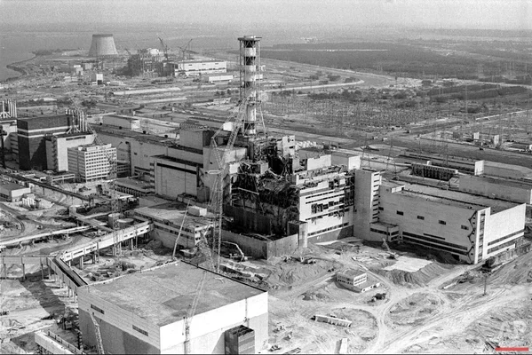 Photographie aérienne en noir et blanc du réacteur n°4 de la centrale nucléaire de Tchernobyl ravagé par l'explosion et l'incendie du 26 avril 1986, débris éparpillés autour de la structure détruite et des bâtiments voisins.