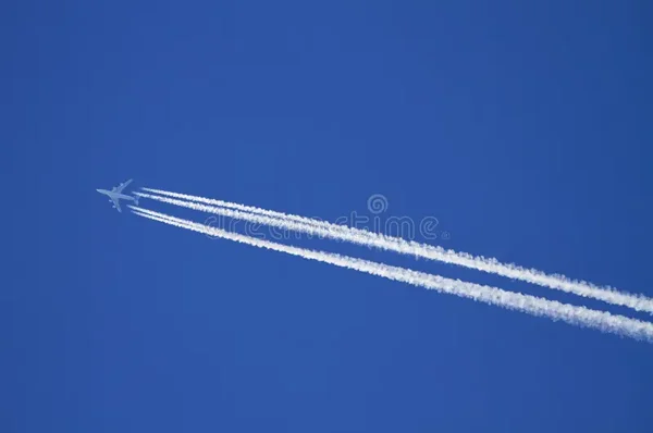 Un avion en vol laissant derrière lui de longues traînées de condensation blanches dans le ciel.