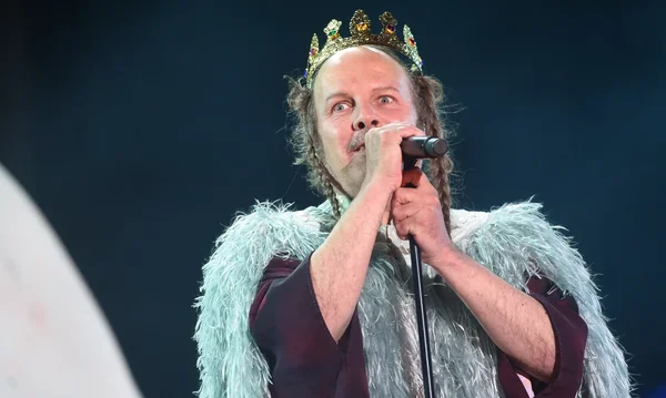 Philippe Katerine se produit sur une scène sombre de l’Hyper Weekend Festival, coiffé d’une couronne bijou, avec une cape bleu clair duveteuse et une tunique bordeaux, tenant un pied de micro près du visage.