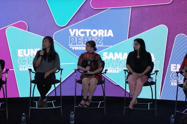 Trois femmes assises sur des tabourets lors d'une table ronde sur les femmes dans l'industrie du jeu vidéo, tenant chacune un micro devant un décor coloré affichant les noms des intervenantes