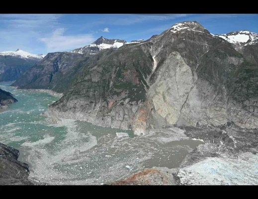 Fjord glaciaire de l'Alaska bordé de montagnes rocheuses enneigées, avec des blocs de glace flottant sur une eau bleue, lieu étudié après un glissement de terrain et un tsunami en 2025.