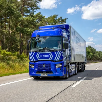 Le Renault T E-Tech électrique bleu de Renault Trucks tractant une remorque blanche portant l'inscription "THIS TRUCK IS 100% ELECTRIC", sur une autoroute bordée de pins