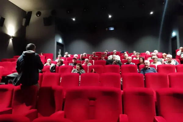 À Riom, des spectateurs assis dans les rangées arrière d'une salle de cinéma aux fauteuils rouges écoutent une personne en veste à capuche qui prend la parole à l'avant.