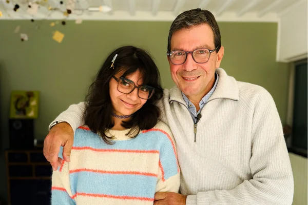 Jean-Marc Laurent, premier « papa Dépakine » à porter plainte contre Sanofi, portant des lunettes et un pull zippé clair, pose le bras autour d'une jeune personne en pull crème à rayures.