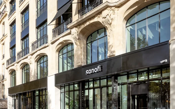 Façade du siège mondial de Sanofi à Paris, avec une enseigne blanche lumineuse au-dessus de vitrines noires, dans un immeuble en pierre aux fenêtres cintrées.