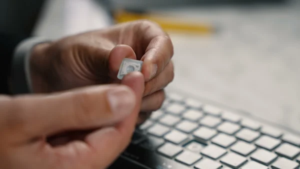 Une personne tient une petite carte SIM devant un clavier d'ordinateur portable, avec un crayon flou en arrière-plan sur un bureau.