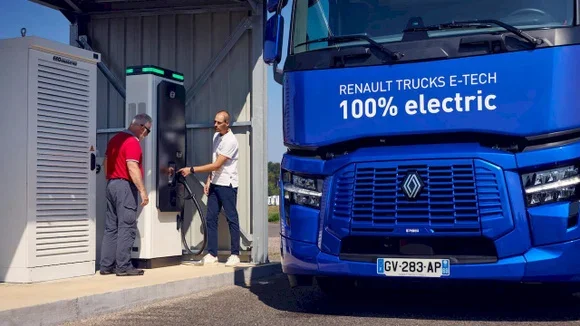 Un camion semi-remorque Renault Trucks E-TECH 100% electric bleu, à l'arrêt sur une aire de recharge, deux hommes se tenant près de la borne de recharge installée sur le corridor de fret européen