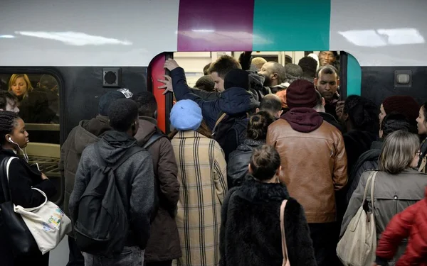Des voyageurs s'entassent pour monter dans une rame de transport francilien ; un homme s'agrippe au chambranle de la porte tandis que d'autres passagers se pressent à l'intérieur.