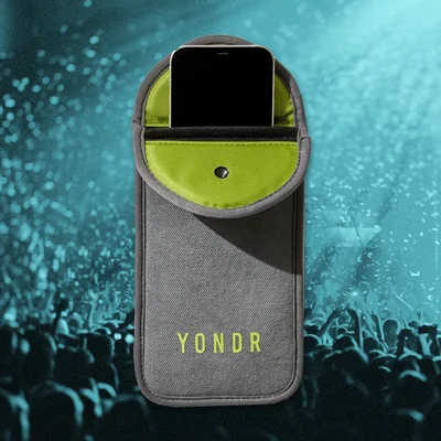 Pochette Yondr grise à intérieur jaune et fermeture verrouillable tenant un smartphone, devant une foule floue aux tons bleu-vert.