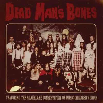 Pochette de l’album Dead Man’s Bones montrant un groupe d’adultes et d’enfants déguisés pour Halloween devant un décor inquiétant.