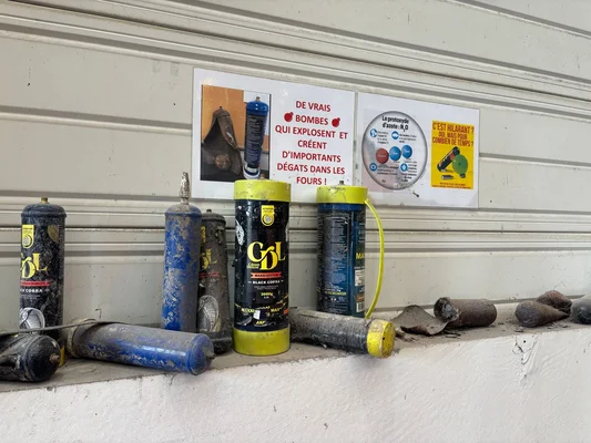 Cartouches et bonbonnes de protoxyde d'azote usagées, dont des modèles des marques GOL et Black Cobra, posées sur un rebord sous des panneaux d'avertissement français sur le risque d'explosion et un protocole N2O.
