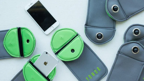 Vue à plat de pochettes Yondr grises et vert néon de type brassard pour téléphone, avec plusieurs iPhone posés à côté et l’un d’eux partiellement glissé dans une pochette ouverte.